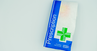 Prescription medication packaging with NHS logo and green cross symbol indicating health services and pharmacy assistance.