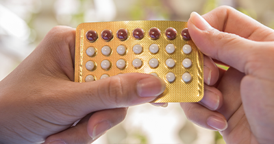 smiling pharmacist in white coat standing in pharmacy with colleagues and shelves of health products including 11 types of medication and advice