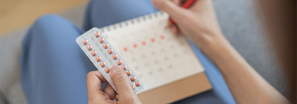 person holding a pack of birth control pills and marking a calendar with red pen showcasing a health schedule for 13 days